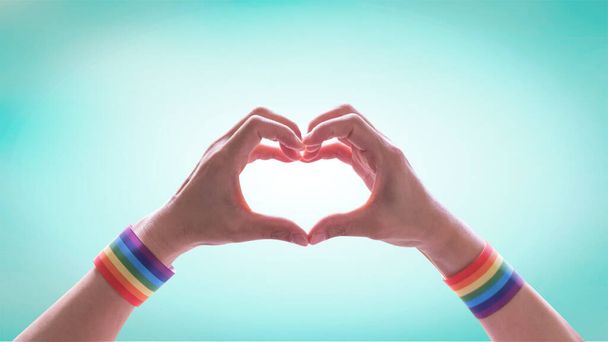 LGBTQの虹の旗のリボンリストバンドを持つLGBTの誇りの月同性愛嫌悪とトランスフォビアに対する国際デーのための人々の心の形の手 - 写真・画像