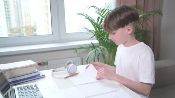 Cute boy leafs through a notebook. The guy is doing homework. - Filmati, video