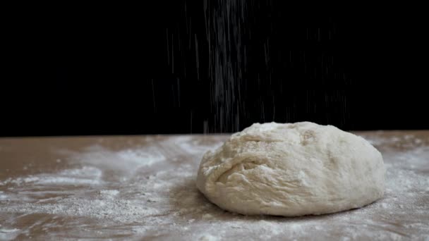 A nyers kenyeret az asztalon fekete alapon történő sütésre készítik elő. A kenyeret liszttel locsolják, hogy ropogós legyen. Ez a videó készült közelről természetes fény 4k - Felvétel, videó