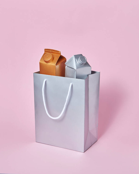 Two mock-up packages for dairy products golden and silver in a paper silver bag on a pastel pink background with soft shadows, copy space. Eco friendly concept. Recycling concept. - Фото, зображення