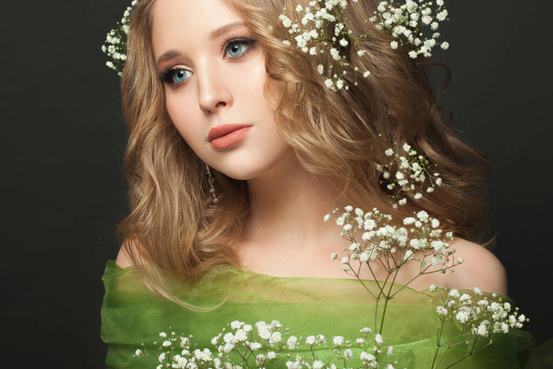 Csinos fiatal nő hosszú, egészséges göndör haj és fehér virágok fekete háttér, gyönyörű arc közelről - Fotó, kép