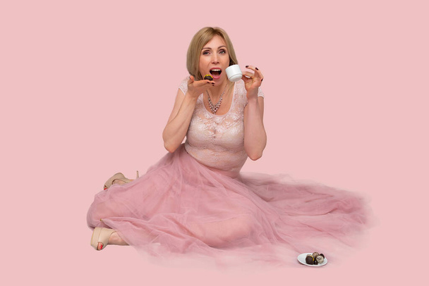 Όμορφη γυναίκα με φλιτζάνι τσάι ή καφέ. Studio πορτρέτο μιας ονειρικής ξανθιάς γυναίκας που φοράει μια ροζ φούστα, κρατώντας ένα φλιτζάνι καφέ και σοκολάτα στα χέρια της, πίνοντας φρέσκο νόστιμο ποτό - Φωτογραφία, εικόνα