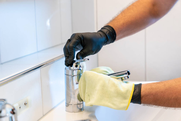 Eine professionelle Reinigungskraft poliert Waschbecken und Wasserhahn mit einem gelben Mikrofasertuch - Foto, Bild