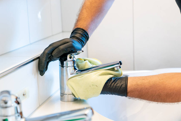 Um limpador profissional polonês uma pia do banheiro e torneira com um pano de micro fibra amarelo
 - Foto, Imagem