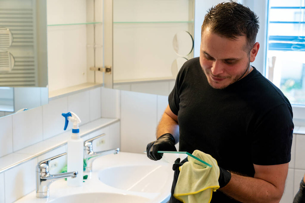 Eine professionelle Reinigungskraft reinigt ein Bad und die Glasregale im Badezimmerschrank - Foto, Bild
