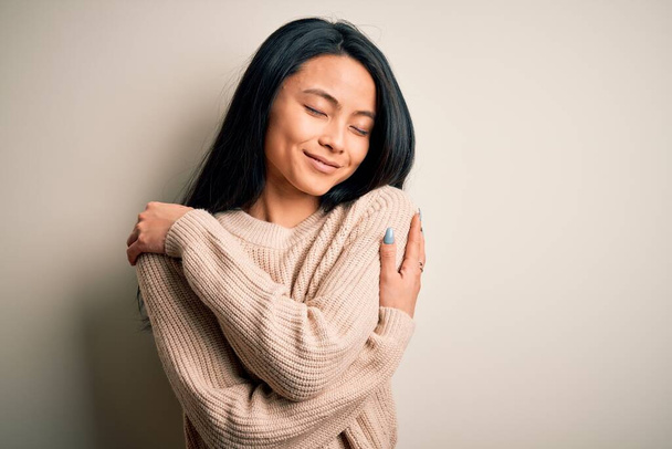 Young beautiful chinese woman wearing casual sweater over isolated white background Hugging oneself happy and positive, smiling confident. Self love and self care - Foto, immagini