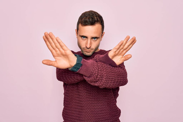Young handsome man with blue eyes wearing casual sweater standing over pink background Rejection expression crossing arms doing negative sign, angry face - Photo, Image
