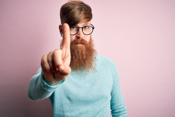 Hezký irský zrzavý muž s vousy a brýlemi přes růžové izolované pozadí ukazující prstem nahoru a rozzlobeným výrazem, bez gesta - Fotografie, Obrázek