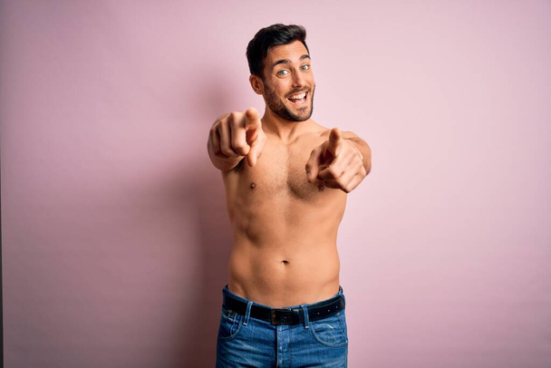 Jeune homme fort beau avec barbe torse nu debout sur fond rose isolé pointant vers vous et la caméra avec les doigts, souriant positif et joyeux
 - Photo, image