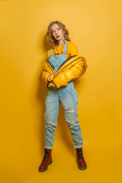 Mooie mode model vrouw in gele winter jas staande op een heldere achtergrond - Foto, afbeelding