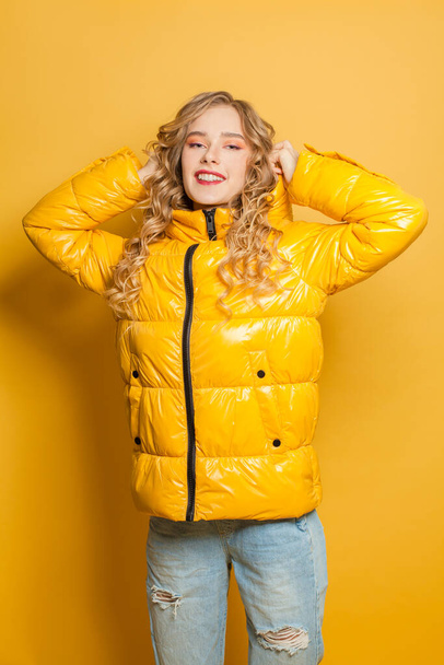Happy pretty model woman in yellow winter jacket posing on bright background - Foto, afbeelding