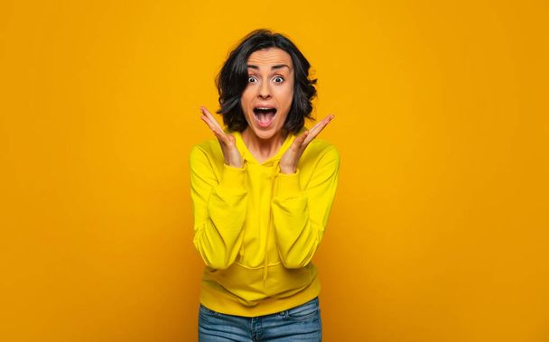 Unexpected win. Half-length photo of excited and happy brunette girl dressed in a yellow hoodie, celebrating unexpected win with her palms opened. - Φωτογραφία, εικόνα