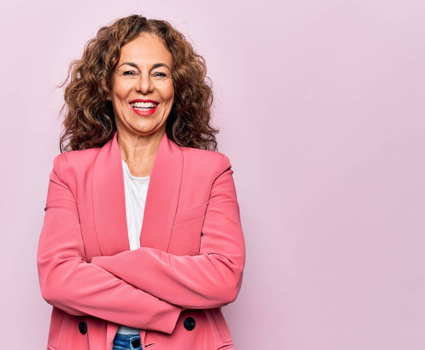 Middle age beautiful businesswoman wearing jacket standing over isolated pink background happy face smiling with crossed arms looking at the camera. Positive person. - Photo, Image