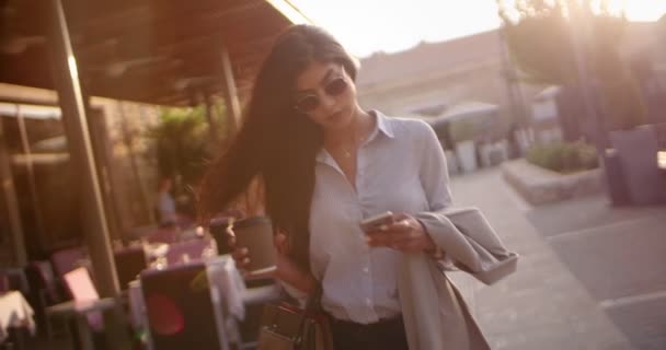 Young businesswoman with coffee walking and texting in the city - Felvétel, videó