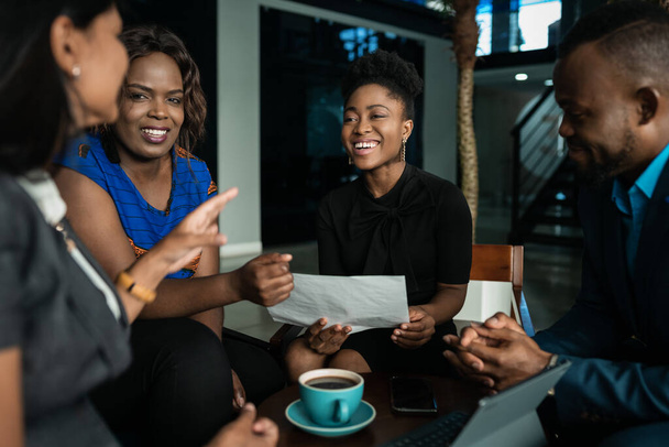 Молоді африканські бізнесмени сміються разом, переглядаючи паперову роботу під час випадкового зібрання в офісі. - Фото, зображення