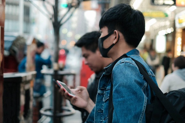 Fiatal ázsiai férfi visel védő arc maszk és keresés a hely és étterem utazni és enni Tokióban, Japán barátaival - Fotó, kép