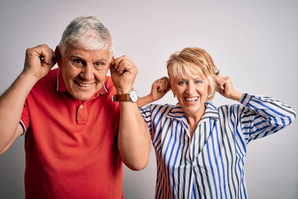 Старша красива пара стоїть разом над ізольованим білим тлом Посміхаючись тягнути вуха пальцями, смішний жест. Проблема прослуховування
 - Фото, зображення