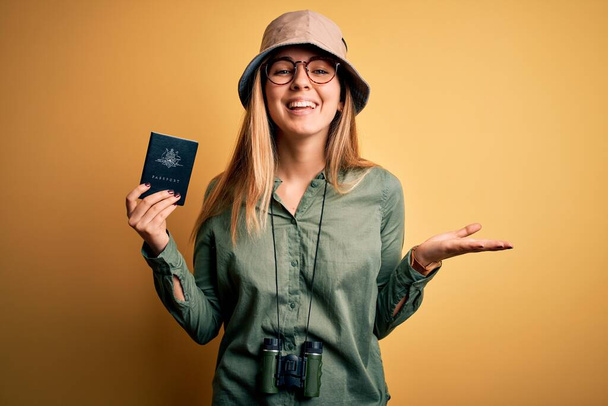 Donna turistica bionda con gli occhi azzurri in vacanza con passaporto australiano usando il binocolo molto felice ed eccitata, espressione vincente che celebra la vittoria urlando con grande sorriso e mani alzate
 - Foto, immagini