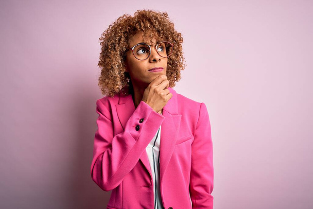 Young african american businesswoman wearing glasses standing over pink background Thinking worried about a question, concerned and nervous with hand on chin - Foto, immagini