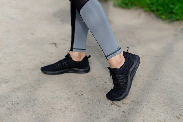 women's feet in grey leggings and black sneakers outdoor - Fotografie, Obrázek