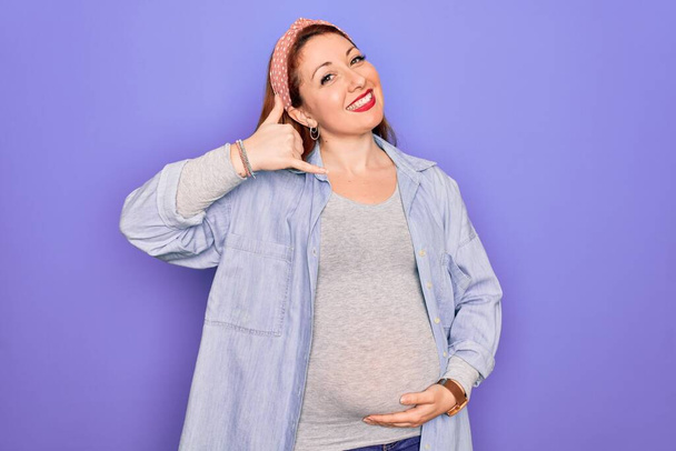 Νεαρή όμορφη κοκκινομάλλα έγκυος γυναίκα περιμένει μωρό πάνω από απομονωμένο μωβ φόντο χαμογελώντας κάνει τηλεφωνική χειρονομία με το χέρι και τα δάχτυλα σαν να μιλάμε στο τηλέφωνο. Επικοινωνία εννοιών. - Φωτογραφία, εικόνα
