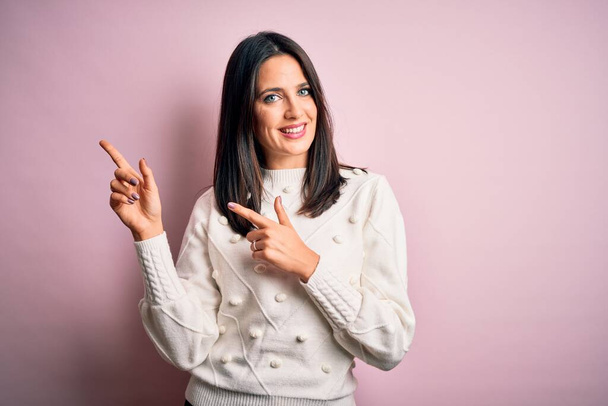 Young brunette woman with blue eyes wearing casual sweater over isolated pink background smiling and looking at the camera pointing with two hands and fingers to the side. - Φωτογραφία, εικόνα