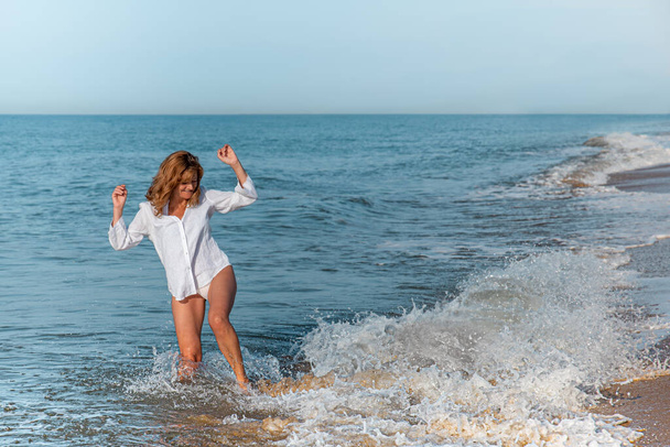 vrouw springen een golf op het strand in een wit shirt  - Foto, afbeelding