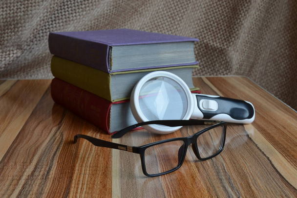 on the table are books, a magnifier and glasses - Photo, Image