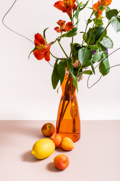 floral composition with roses and red Alstroemeria in wires in orange vase near lemon and apricots isolated on white - Photo, image