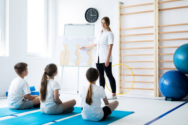 Young physical therapist talking with kids about bad postures - Foto, imagen