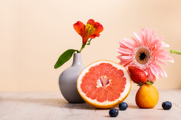 floral and fruit composition with Alstroemeria, gerbera, berries, grapefruit and apricot on wooden surface isolated on beige - Photo, Image