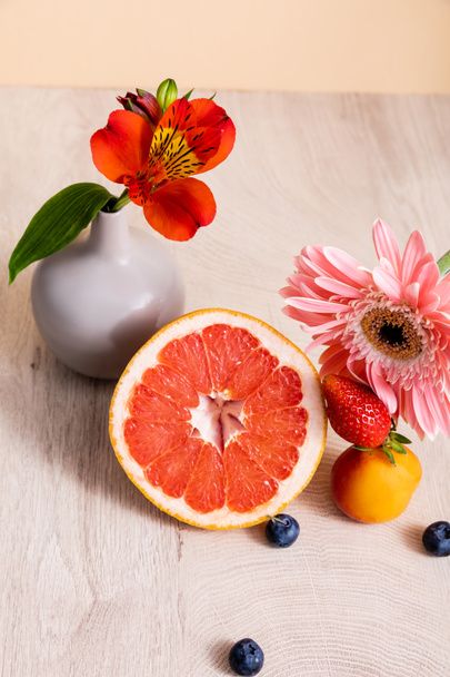 цветочный и фруктовый состав с альстромерией, герберой, ягодами, грейпфрутом и абрикосом на деревянной поверхности, изолированной на бежевом
 - Фото, изображение