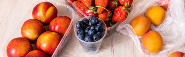 fruit composition with blueberries, strawberries, nectarines and peaches in plastic containers on wooden surface, panoramic crop - Photo, Image