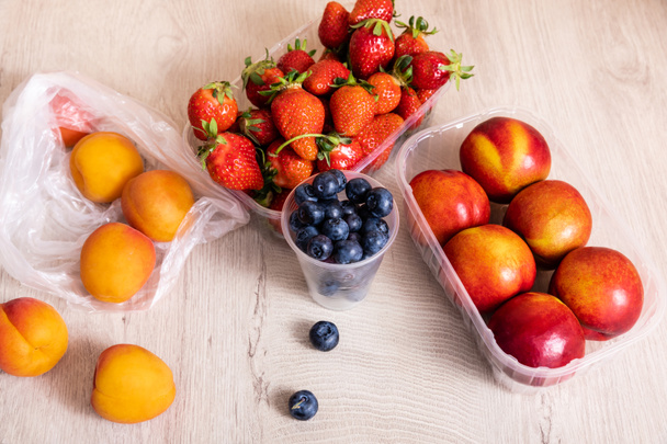 fruit composition with blueberries, strawberries, nectarines and peaches in plastic containers on wooden surface - Photo, Image
