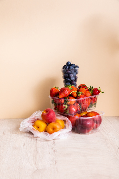 composição de frutos com mirtilos, morangos, nectarinas e pêssegos em recipientes de plástico sobre superfície de madeira sobre fundo bege
 - Foto, Imagem