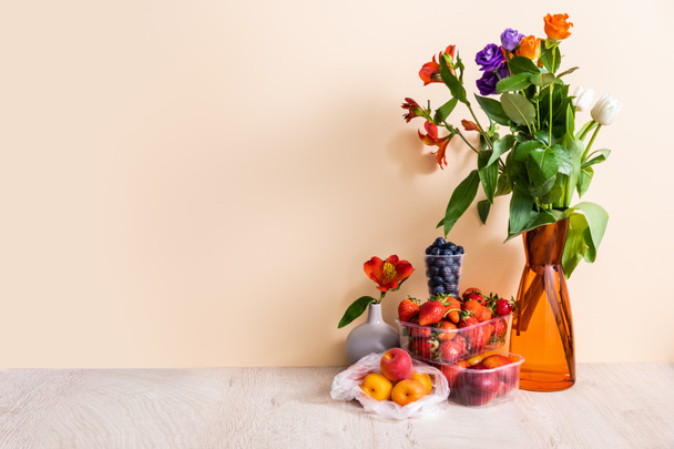 bloem- en fruitcompositie met boeket in vaas en zomerfruit op houten ondergrond op beige ondergrond - Foto, afbeelding