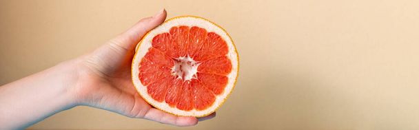обрізаний вид жіночої руки з соковитим грейпфрутом наполовину на бежевому фоні, панорамний урожай
 - Фото, зображення