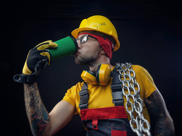 mężczyzna w kombinezonie budowlanym z metalowym łańcuchem pije drinka - Zdjęcie, obraz