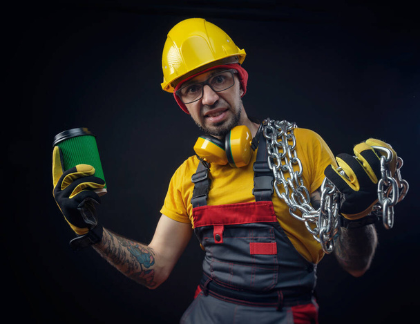ein Mann im Baufirma-Overall mit Metallkette und Kaffeetasse - Foto, Bild