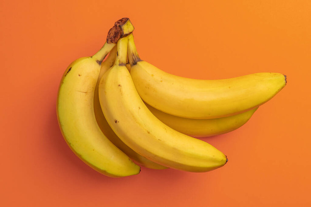 Joukko kypsiä banaaneja kirkkaan oranssilla taustalla. Täplikäs ylikypsä hedelmä. Näkymä ylhäältä. Tiivistelmä - Valokuva, kuva