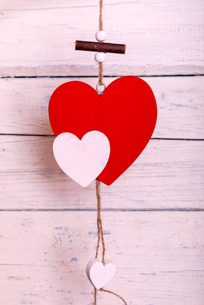 Un romántico corazón de madera colgando de tablas blancas pintadas. Corazones entregando la cuerda. Tarjeta de felicitación de San Valentín. Concepto de amor
 - Foto, imagen