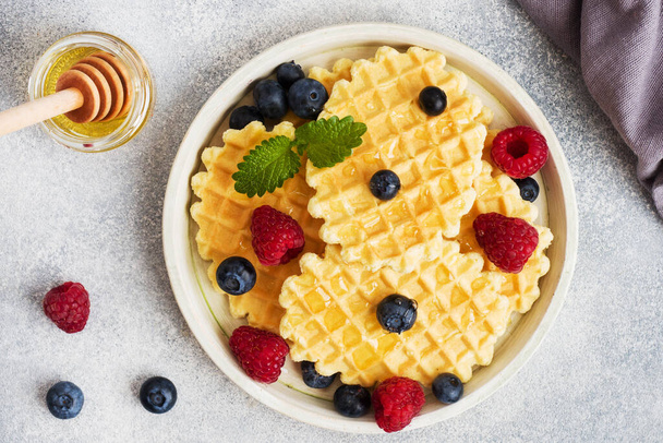 Corrugated waffle cookies with fresh raspberries and blueberries on a concrete background. Copy space - Zdjęcie, obraz