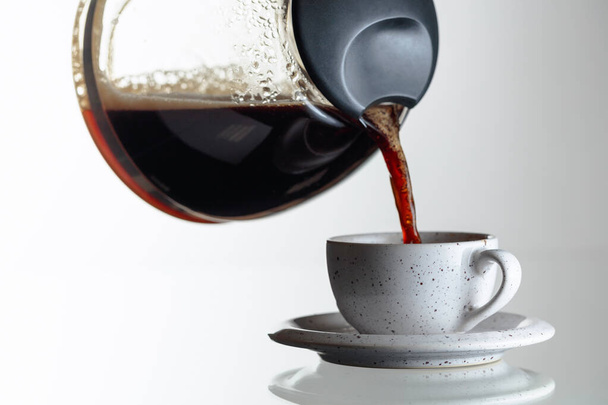 Черный кофе в керамической чашке на стеклянном столе. Кофе наливают из кофеварки в чашку. Копирование пространства. - Фото, изображение