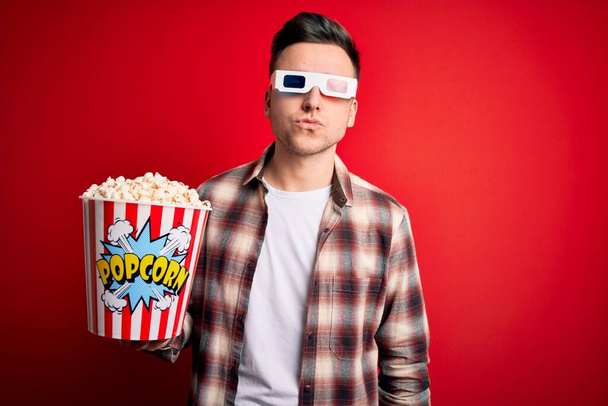 Young handsome caucasian man wearing 3d movie glasses and eating popcorn looking at the camera blowing a kiss on air being lovely and sexy. Love expression. - Foto, Bild