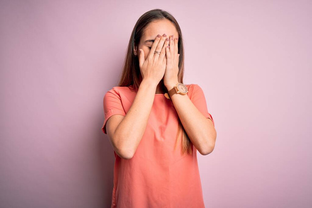 Young beautiful woman wearing casual t-shirt standing over isolated pink background with sad expression covering face with hands while crying. Depression concept. - Foto, afbeelding