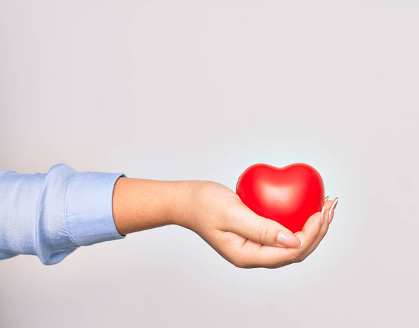Χέρι καυκάσιας νεαρής γυναίκας που κρατά κόκκινη καρδιά πάνω από απομονωμένο λευκό φόντο - Φωτογραφία, εικόνα