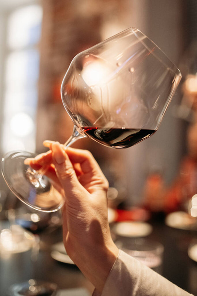 main féminine tient un verre avec du vin rouge lors d'une dégustation dans un bar à vin
 - Photo, image