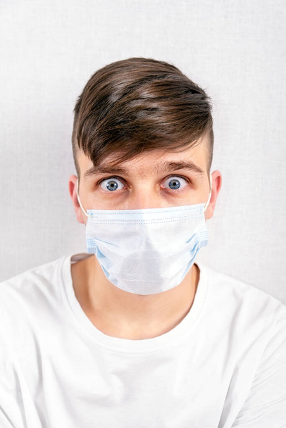 Shocked Young Man in a Flu Mask by the White Wall closeup - Фото, изображение