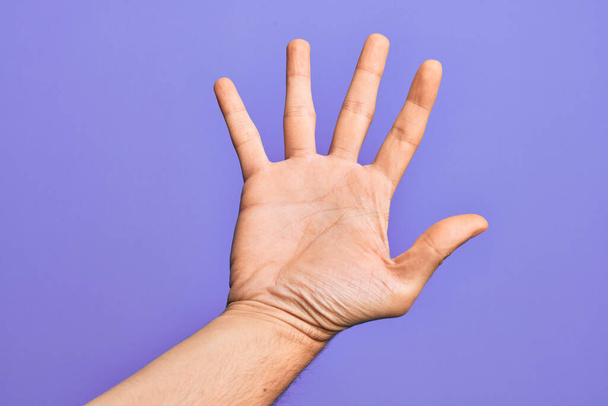 Ruka bělocha mladý muž ukazující prsty přes izolované fialové pozadí počítání číslo 5 ukazující pět prstů - Fotografie, Obrázek