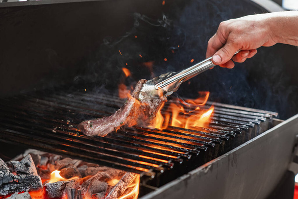 Muž smaží grilovaný hovězí steak s plamenama - Fotografie, Obrázek